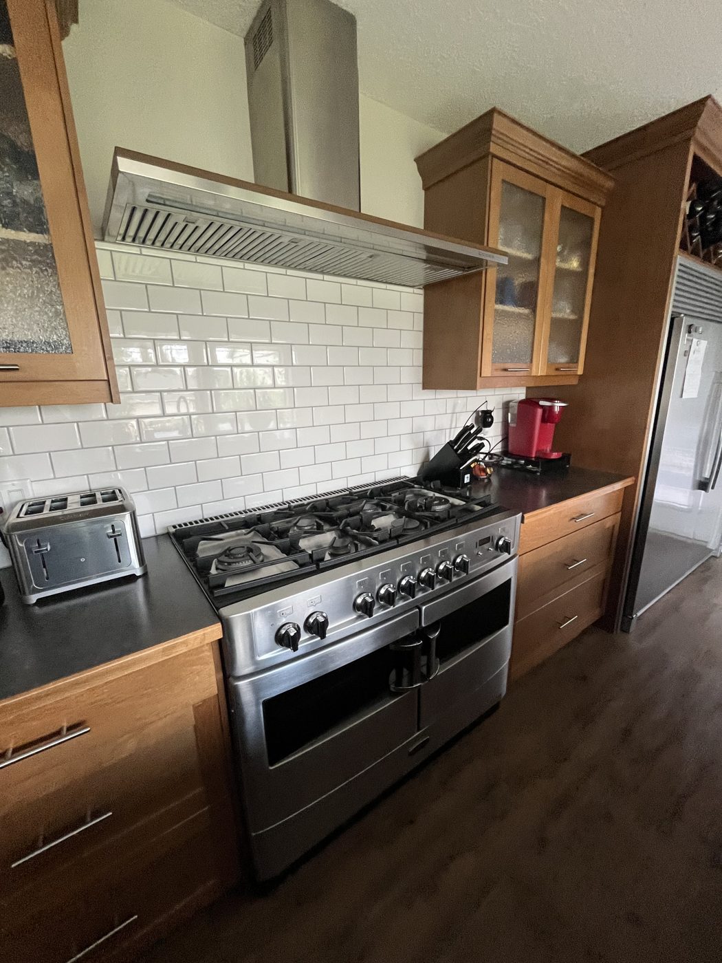 Clean kitchen with gleaming gas range, range hood and white subway tile